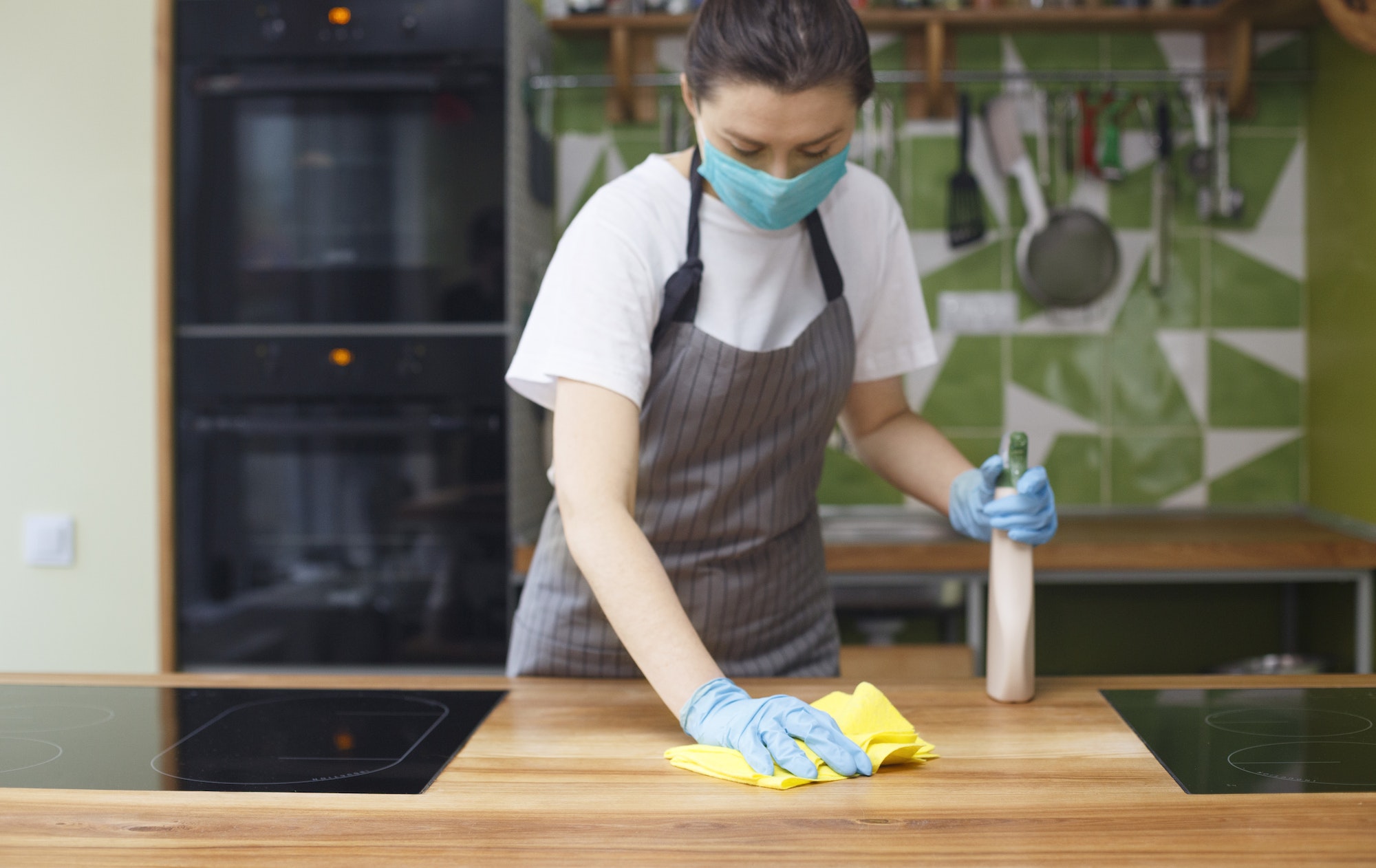 Woman cleaning kitchen with disinfecting spray and microfiber